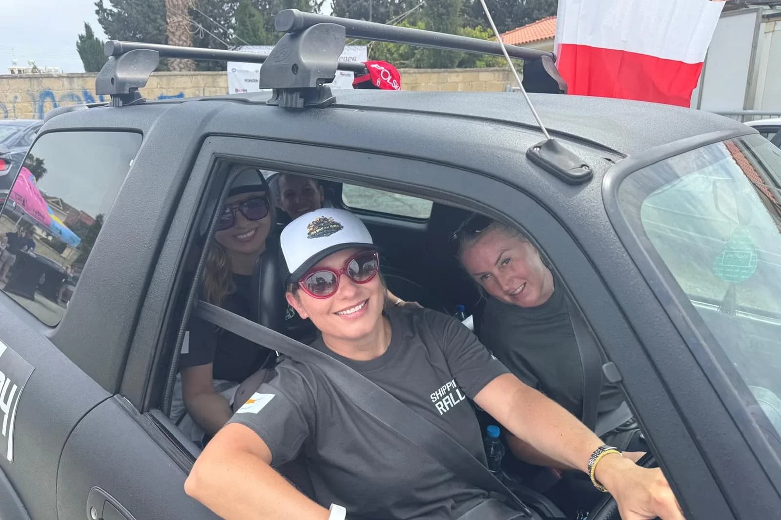 A team grinning from the cab of their rally car at the start line